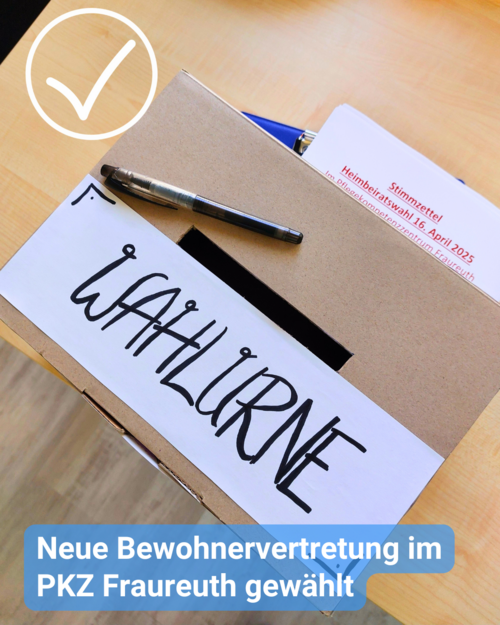 Nahaufnahme einer Karton-Wahlurne mit einem weißen Schild darauf, auf dem in großen, schwarzen, handgeschriebenen Buchstaben „WAHLURNE“ steht.   Ein Stift und ein teilweise sichtbares Stück Papier mit Text liegen auf der Box. Das Papier scheint einen Stimmzettel oder ein Informationsblatt zur Wahl zu zeigen, auf dem ein Teil des deutschen Textes zu erkennen ist, darunter „Heimbeiratswahl 16. April 2025“.   Am unteren Rand des Bildes überlagert ein hellblaues Banner die Szene und verkündet: „Neue Bewohnervertretung im PKZ Fraureuth gewählt“. Oben links ist ein Häkchen dargestellt. Der Hintergrund deutet auf einen Holztisch hin.